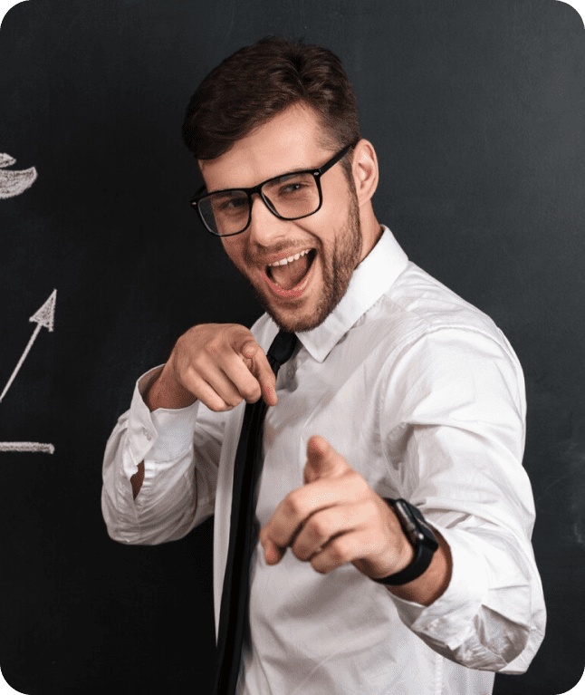 Smiling man pointing at camera in front of chalkboard.