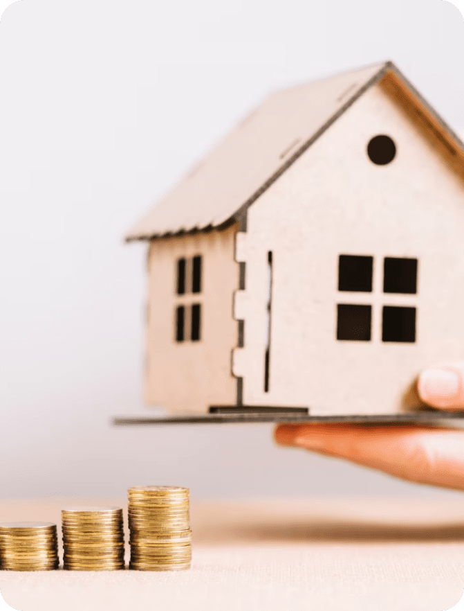 Hand holding model house over coins.