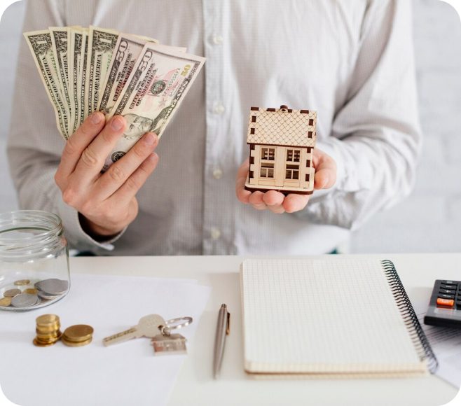 Person holding cash and a house model.