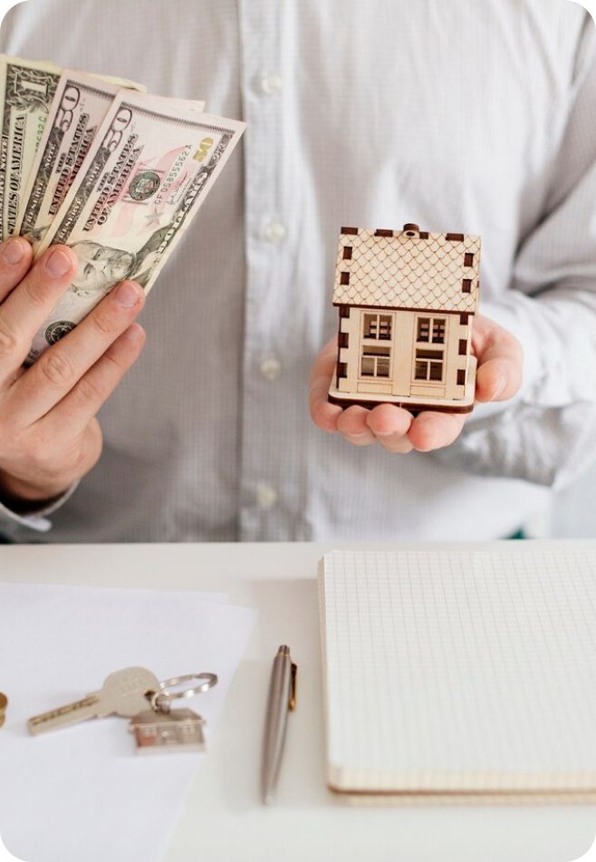 Person holding cash and a house model.