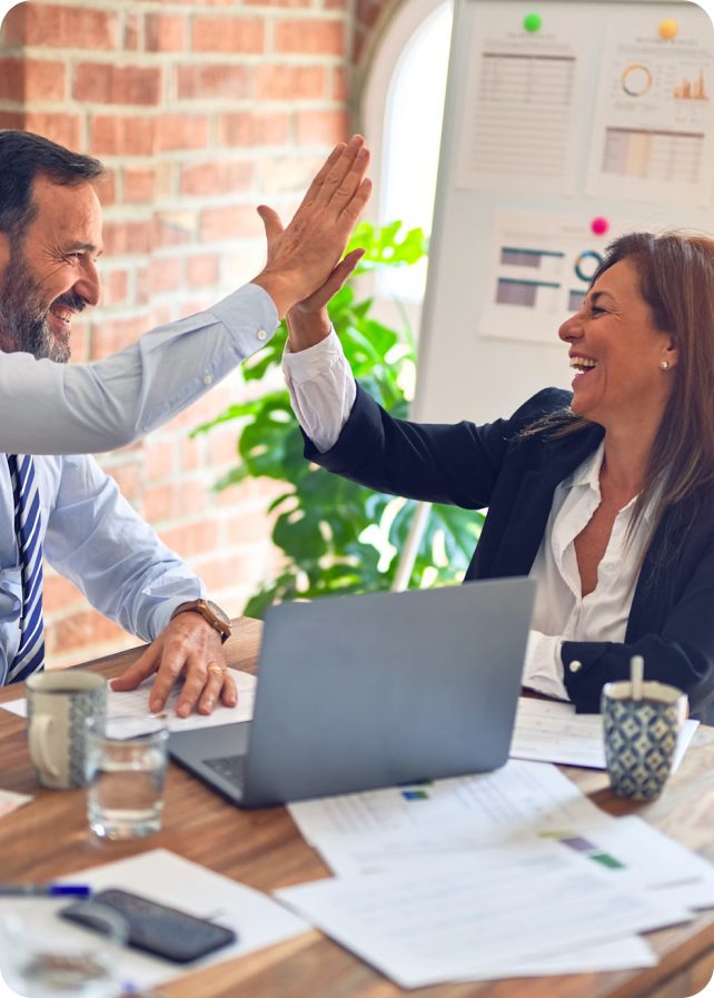 Two colleagues high five at their desk.